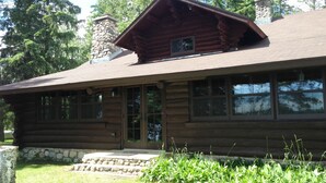 Une cabane en rondins avec une cheminée en pierre, de grandes fenêtres et des fondations en pierre.