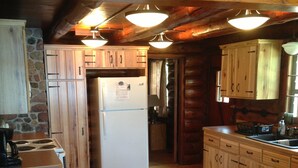 Une cuisine rustique avec des meubles en bois, un réfrigérateur blanc et une cuisinière. Le sol est recouvert de tapis noirs et le plafond est orné de poutres en bois.