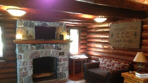 L’intérieur d’une cabane en rondins, avec une cheminée en pierre, un canapé, une petite table et une lampe.