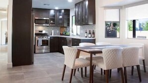 A modern kitchen with dark cabinets, stainless steel appliances, and a dining area with a white table and chairs.