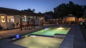 A swimming pool with a patio area, a covered seating area, and a building with a cactus decoration.