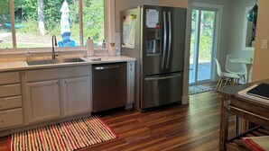 A modern kitchen with a stainless steel refrigerator, a built-in dishwasher, and a window overlooking a garden. - The Bay View Brick --Stunning View of Bay 
 (Traverse City)