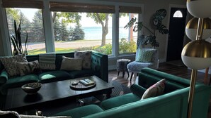 A living room with a green sofa, a coffee table, and a view of the outdoors. - The Bay View Brick --Stunning View of Bay 
 (Traverse City)