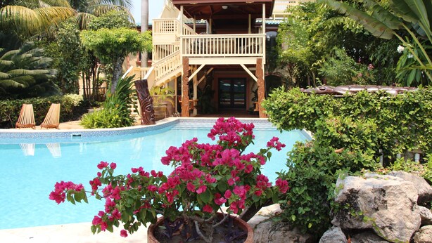A pool area with a two-story building, a balcony, and lush greenery. - Paradise Found!  Beautiful Private Villa On The Sea in the Village of Placencia! (Placencia Village)