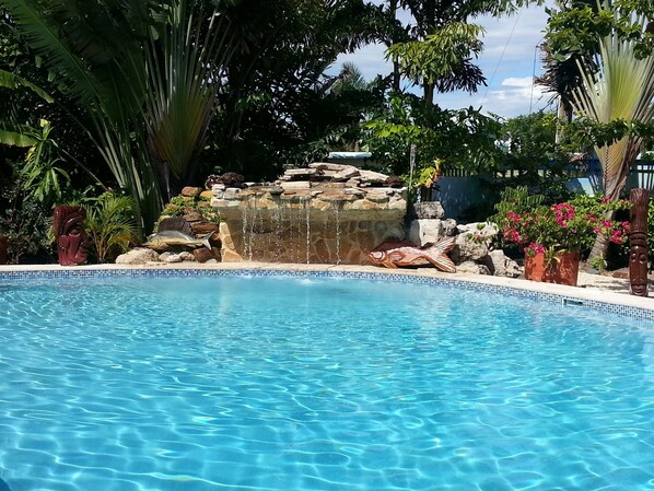 Una piscina azul cristalina con una cascada y esculturas decorativas de peces.