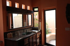 Un baño con un espejo grande, un lavamanos con una pila decorativa y vistas a un área exterior a través de una puerta de vidrio.
