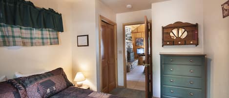 Une chambre à coucher comprenant un lit, une commode, une fenêtre avec des rideaux et une porte donnant sur une autre pièce.