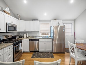 A modern kitchen with white cabinets, stainless steel appliances, and a dining area with a wooden table and chairs.