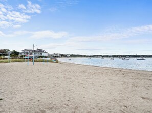 A beach with a volleyball net, a house, and boats on the water.