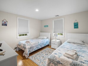 Un dormitorio con dos camas, una mesita de noche, un escritorio y una ventana con persianas.