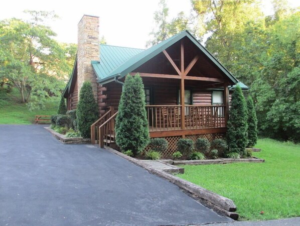 Situated among evergreen trees, this cabin features a wooden deck and a charming chimney.