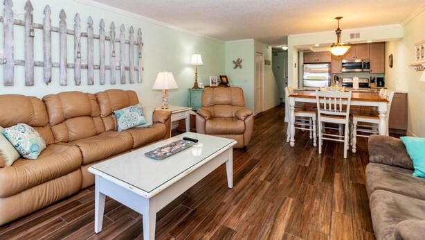 A living room with a brown leather sofa, a white coffee table, and a dining area with a wooden table and chairs. - Ponce Landing 7 (Saint Augustine)