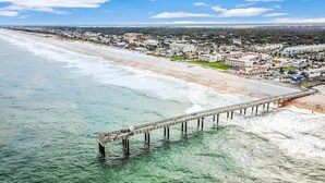 An aerial view of a coastal town with a long pier extending into the sea, a beach, and residential buildings. - Ponce Landing 7 - Oceanfront Townhome - Heated Pool (Saint Augustine)