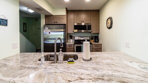 A kitchen with a marble countertop, stainless steel appliances, wooden cabinets, and a wall clock. - Ponce Landing 7 - Oceanfront Townhome - Heated Pool (Saint Augustine)