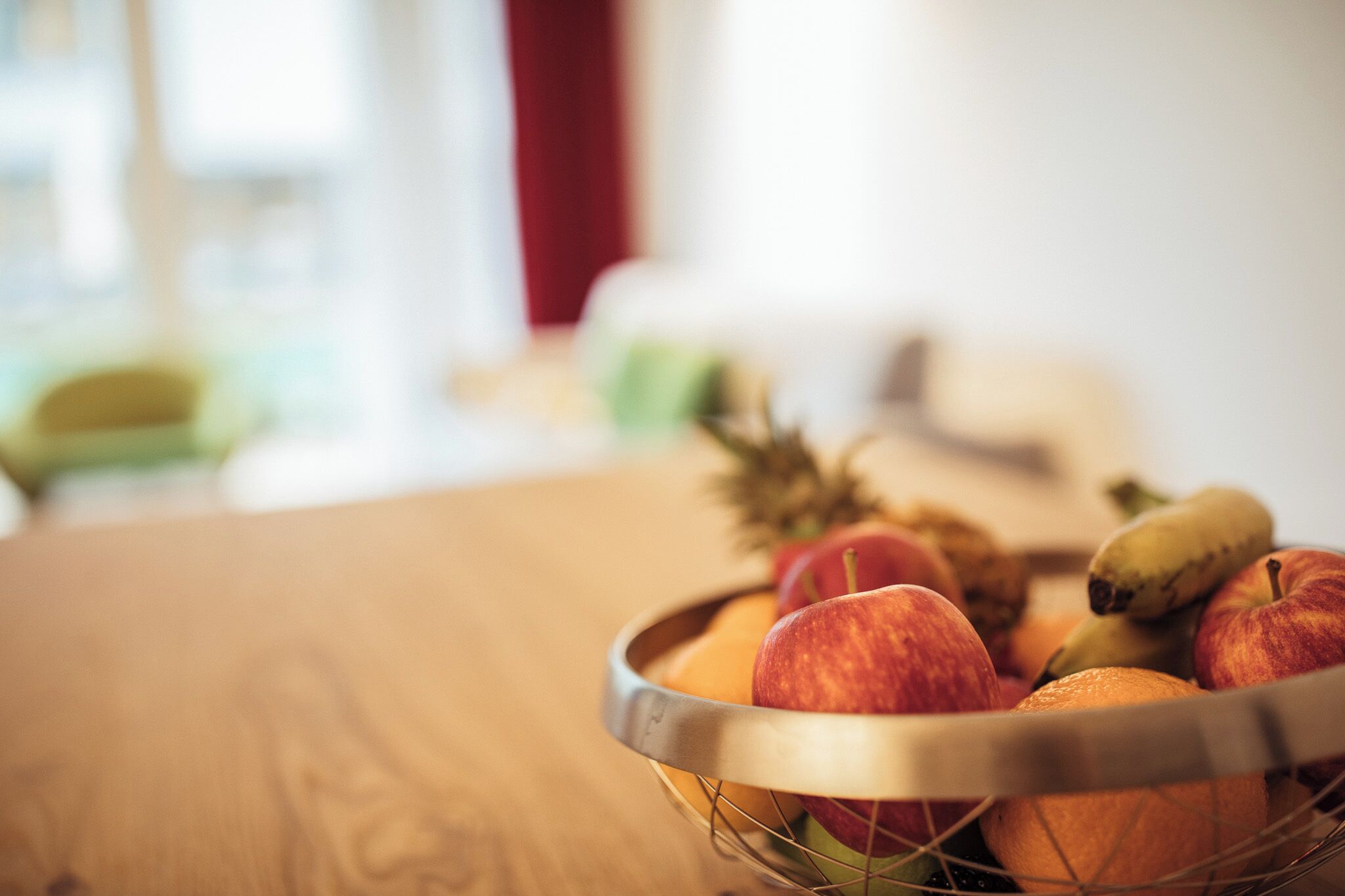 Eine Obstschale auf einem Holztisch mit Äpfeln, Bananen und einer Ananas.