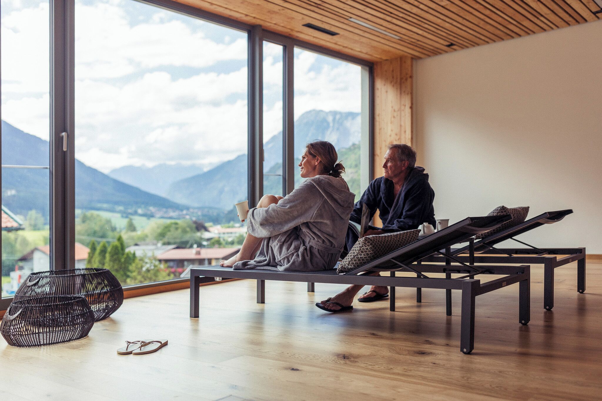 Zwei Personen sitzen auf einer Bank mit Blick auf Berge und eine Stadt.