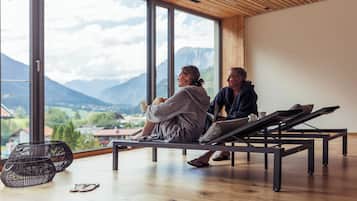 Zwei Personen sitzen auf einer Bank mit Blick auf Berge und eine Stadt.