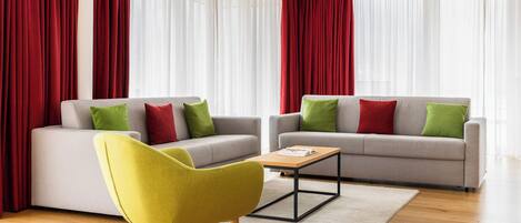 A modern living room with two grey sofas, red curtains, and a yellow armchair.
