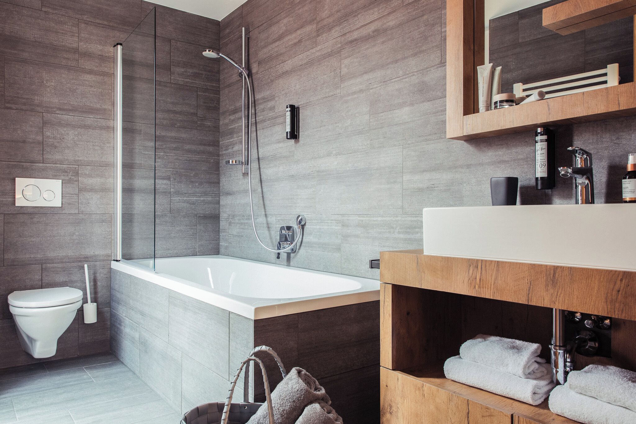 A modern bathroom with a bathtub, shower, toilet, and a vanity with a mirror and shelves.