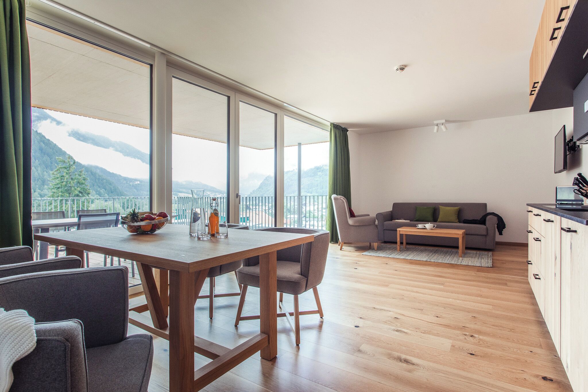 Ein modernes Wohnzimmer mit Essbereich, großen Fenstern und Blick auf die Berge, einer Couch und einer Küchenzeile.