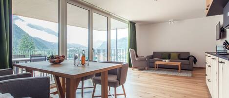 Una sala de estar moderna con comedor, ventanas amplias con vistas a la montaña, un sofá y una zona de cocina.
