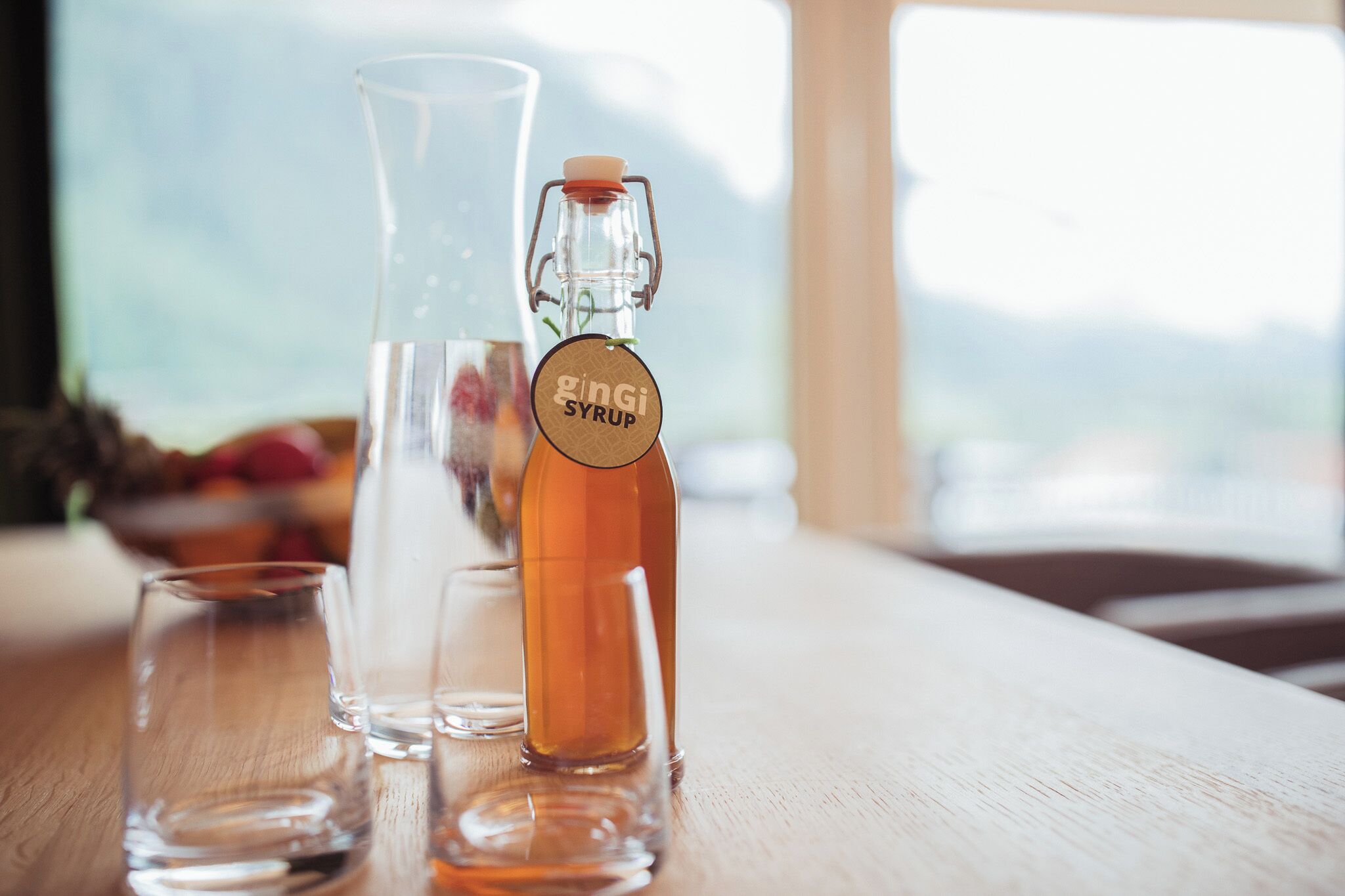 A glass bottle labeled 'gingi syrup' and two clear glasses on a wooden surface.