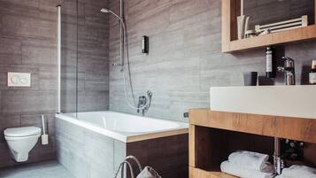 Un baño moderno con bañera, ducha, inodoro y tocador de madera con toallas.