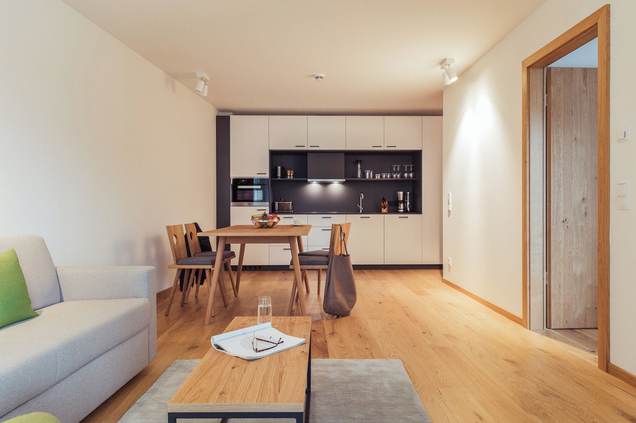 Un salon moderne avec un canapé, une table à manger et des chaises. Au fond, on aperçoit une cuisine équipée de meubles et d’appareils électroménagers.