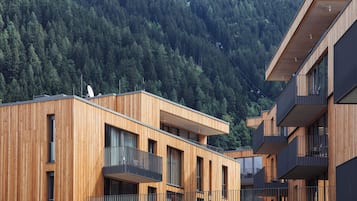 Een modern meerlaags gebouw met houten lambrisering, balkons en een beboste heuvel in de achtergrond.