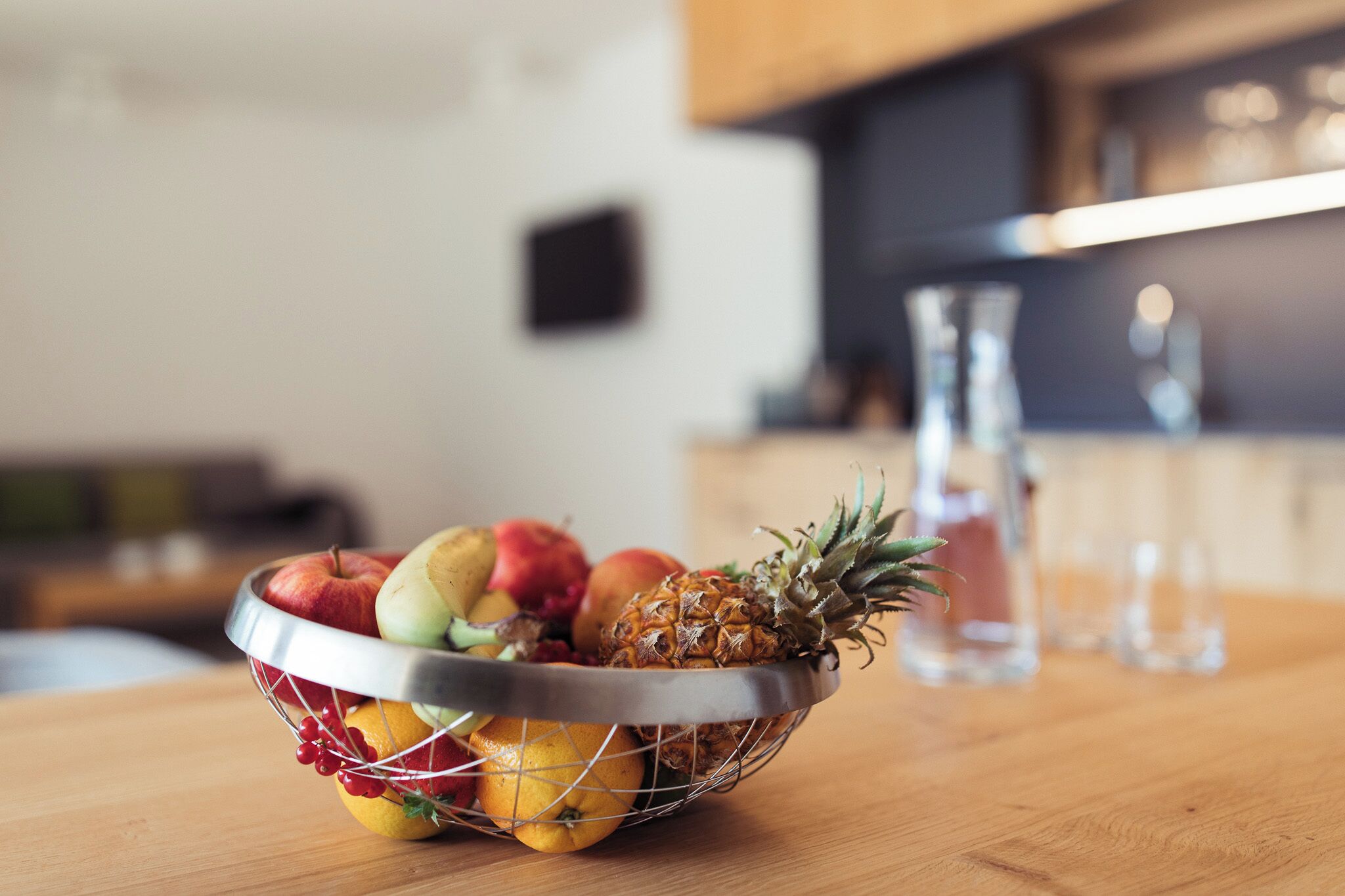 Un panier de fruits sur une table en bois, avec une cuisine en arrière-plan.