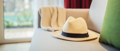 A room with a sofa, a window with a view, and a hat on the sofa.