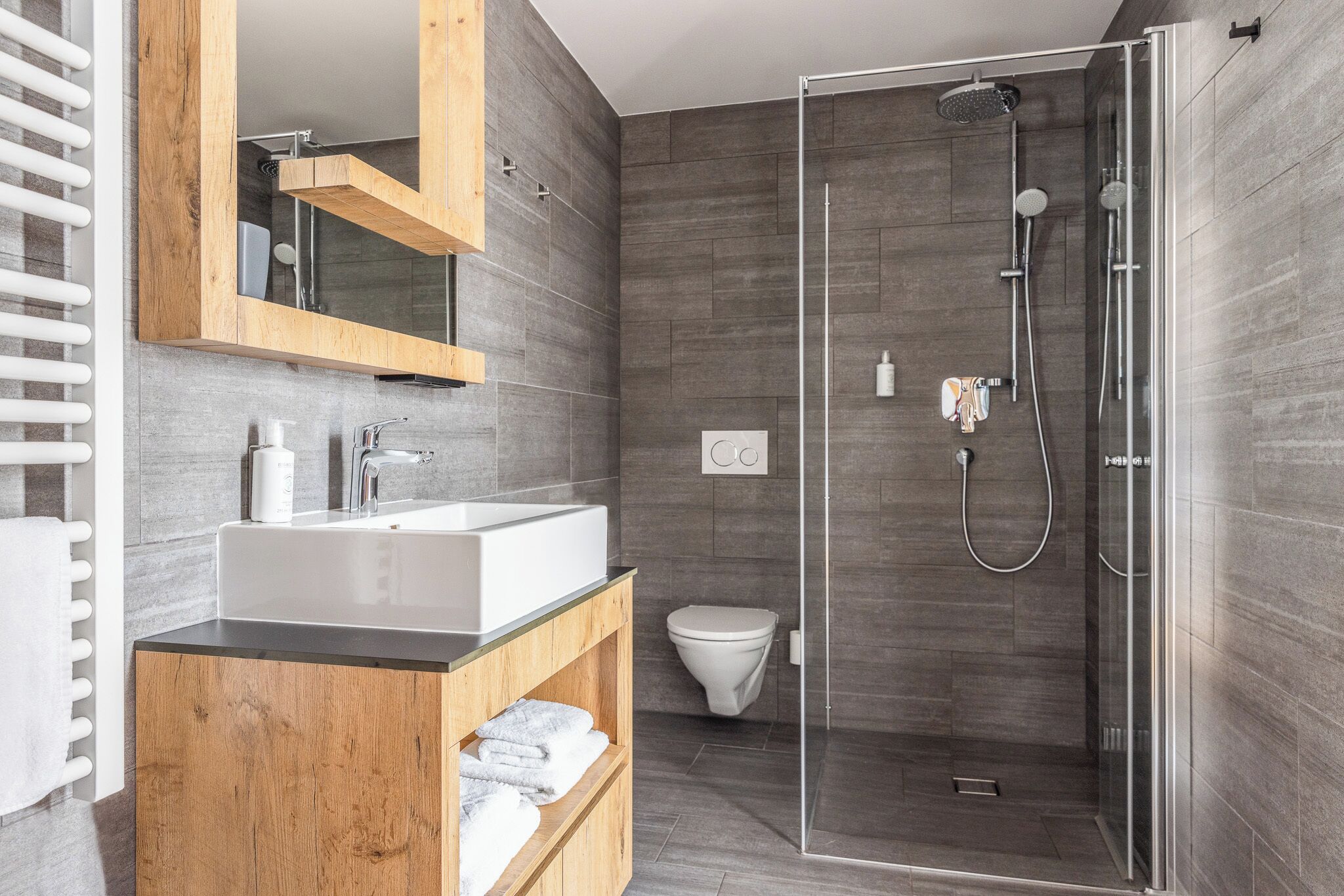 Un baño moderno con ducha envuelta en vidrio, tocador de madera con lavabo y retrete.