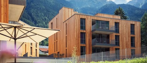A modern building with wooden exterior walls, balconies, and a view of mountains.