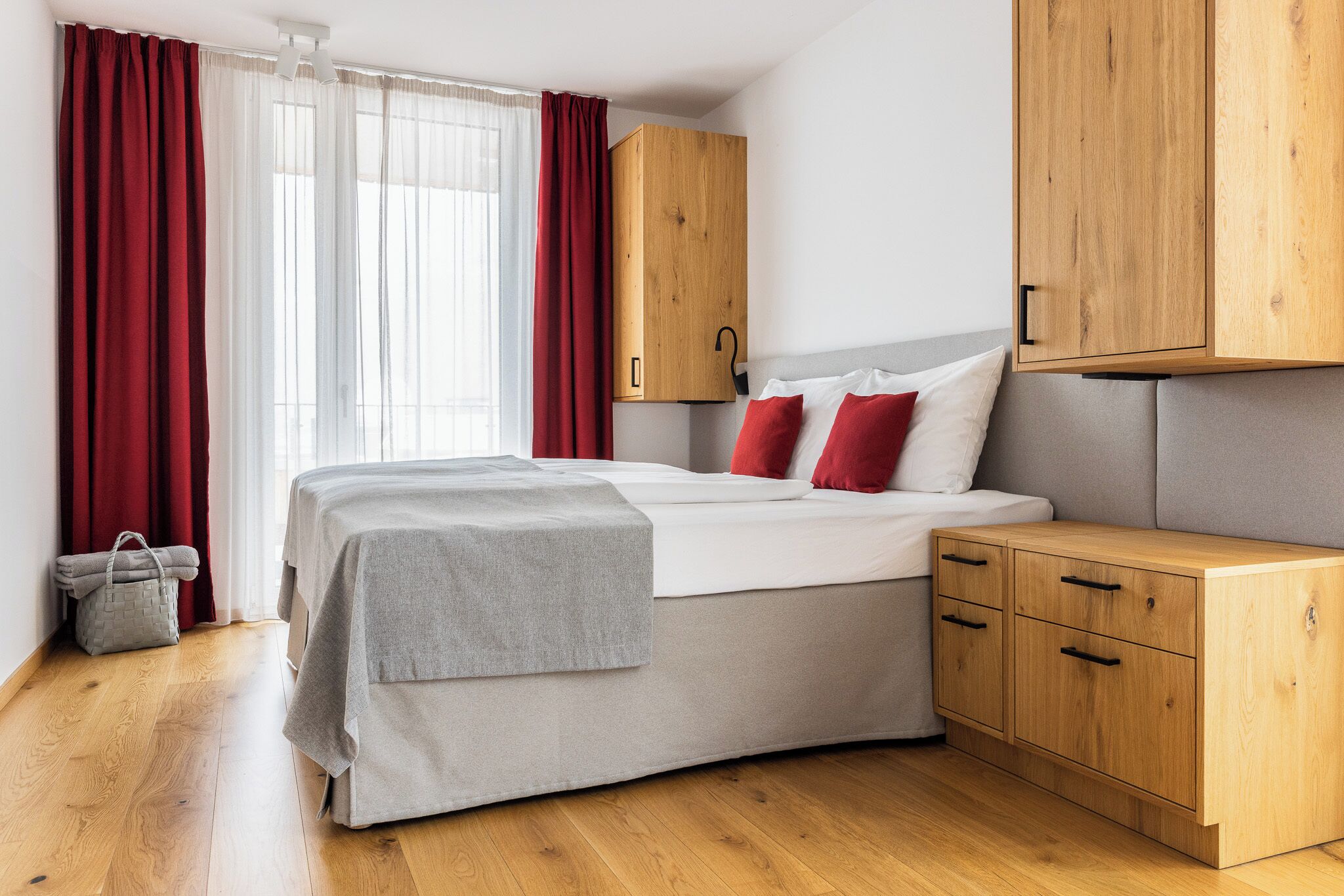Une chambre à coucher avec un lit, des armoires en bois, une couverture grise et un sac à main gris.