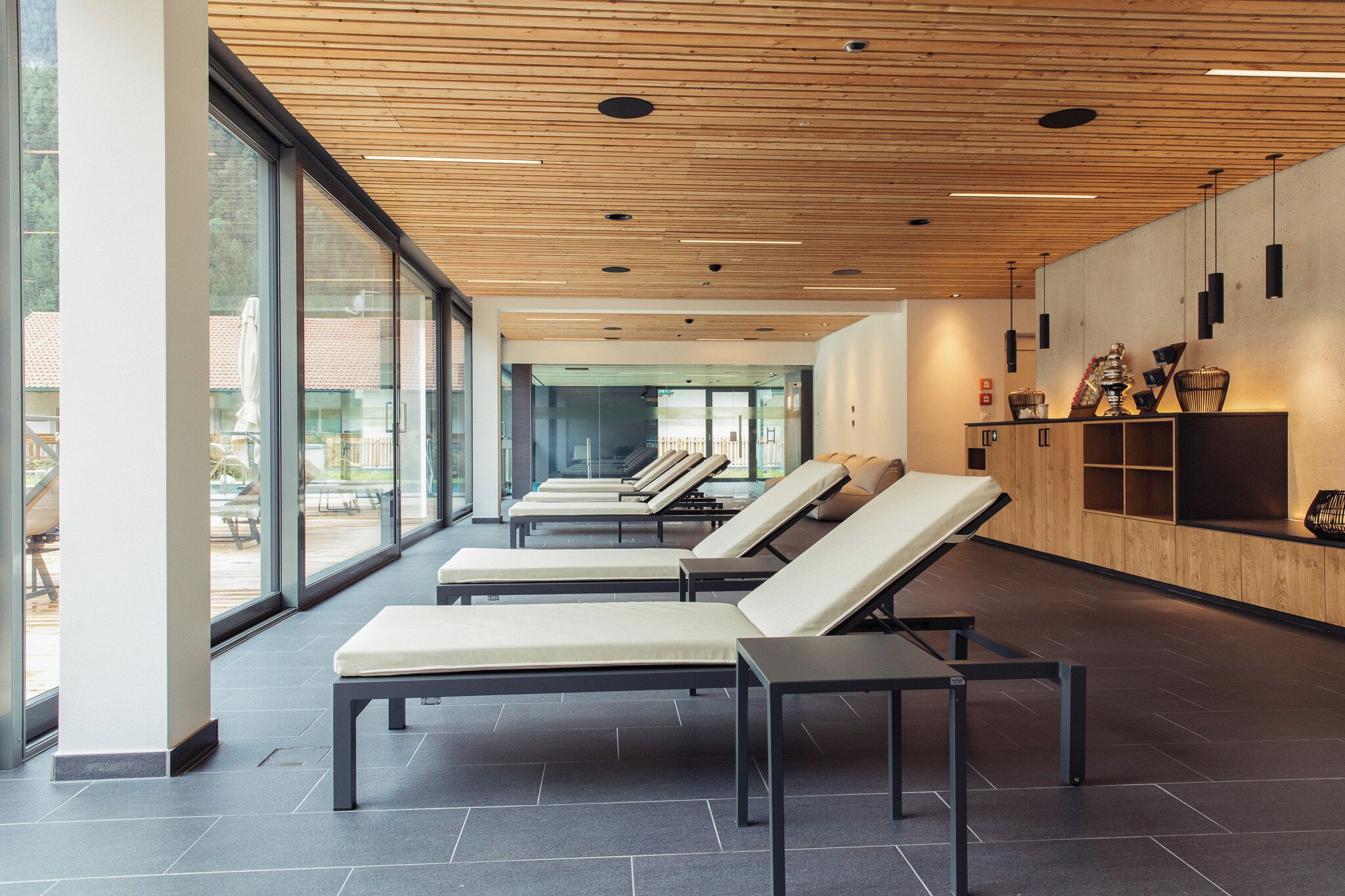 A modern lounge area with reclining chairs and a wooden ceiling, large windows, and a reception desk.