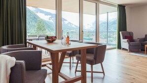 Un espace repas comprenant une table et des chaises, une vue sur les montagnes à travers de grandes fenêtres et un balcon doté d’une balustrade.