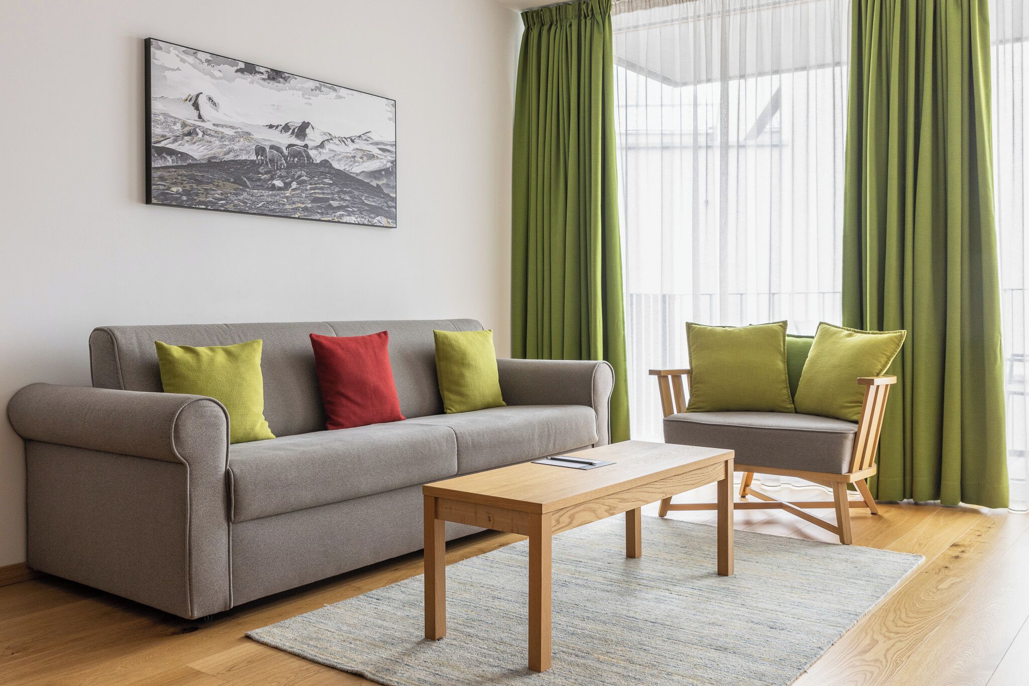 Een moderne woonkamer met een grijze bank, een houten salontafel en een groene fauteuil met passende kussens.