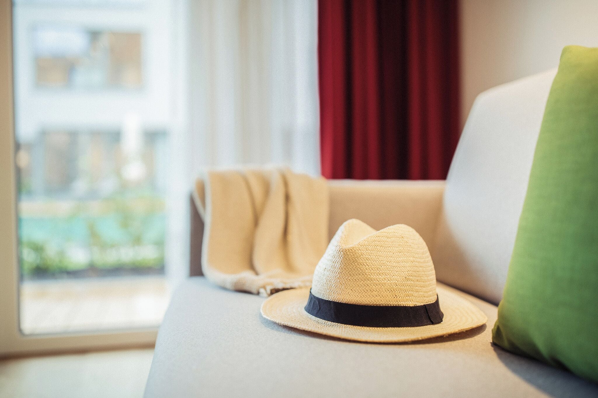 Une pièce avec un canapé, une fenêtre avec des rideaux et un chapeau posé sur le canapé.