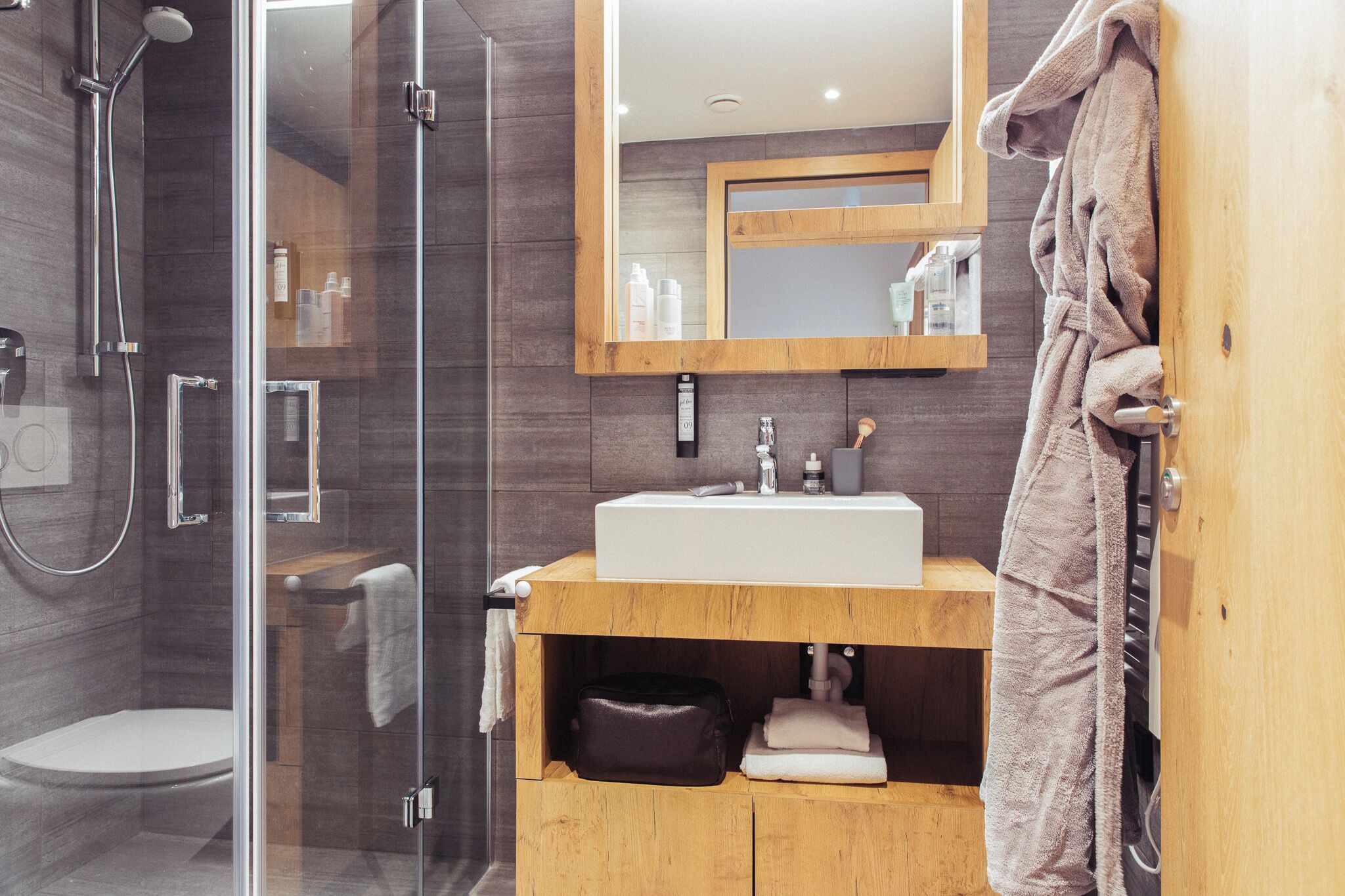 Un bagno moderno con doccia vetro, mobile bagno in legno con lavello e specchio sopra.