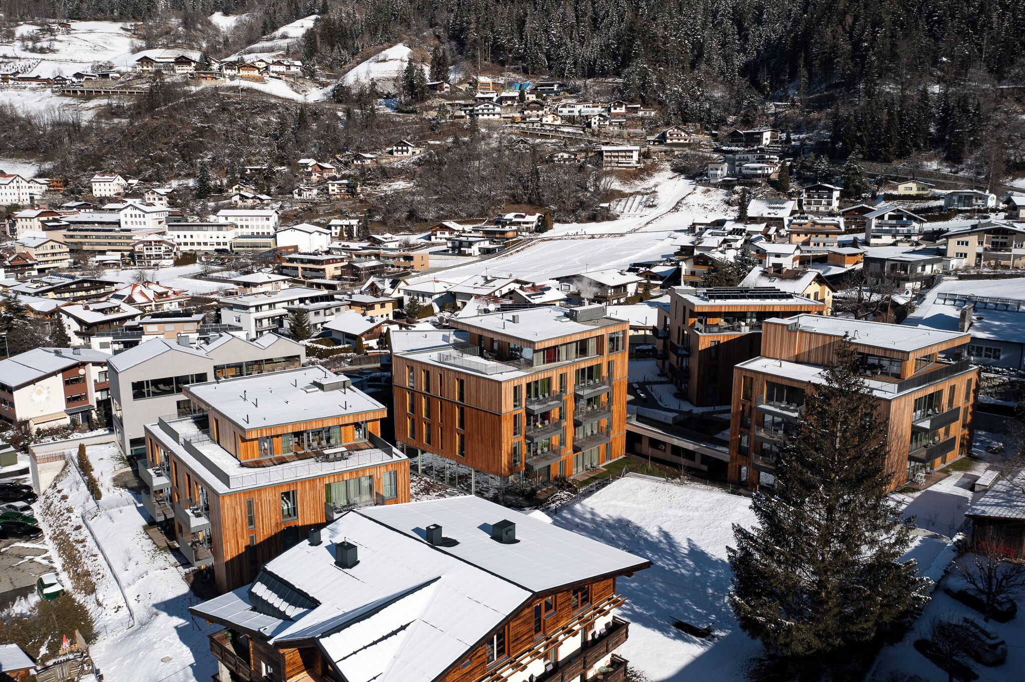 Una zona residencial nevada con edificios modernos, incluyendo una estructura de madera destacada con balcones.