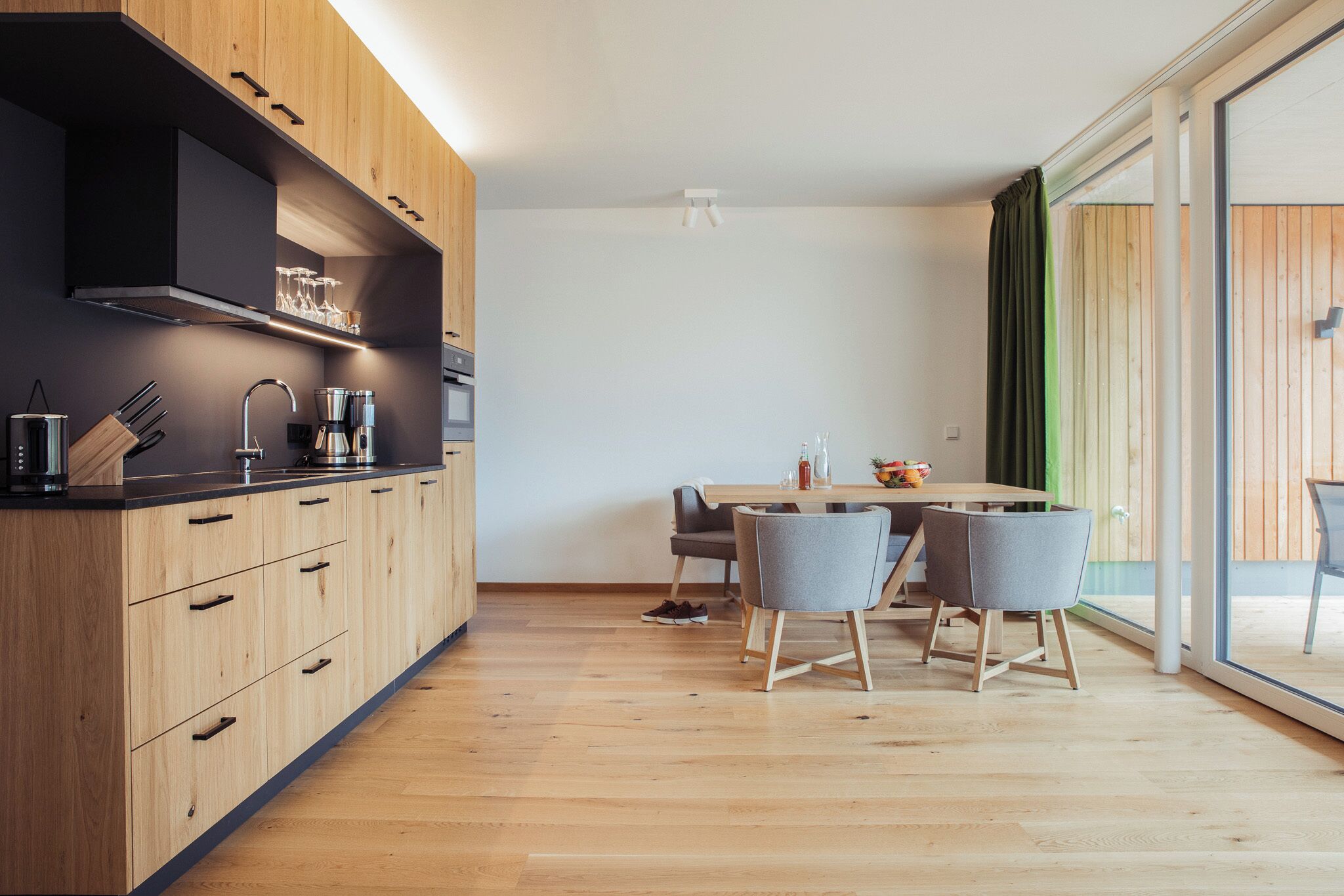 A modern kitchen with wooden cabinets, a built-in oven, and a dining area with a table and chairs.