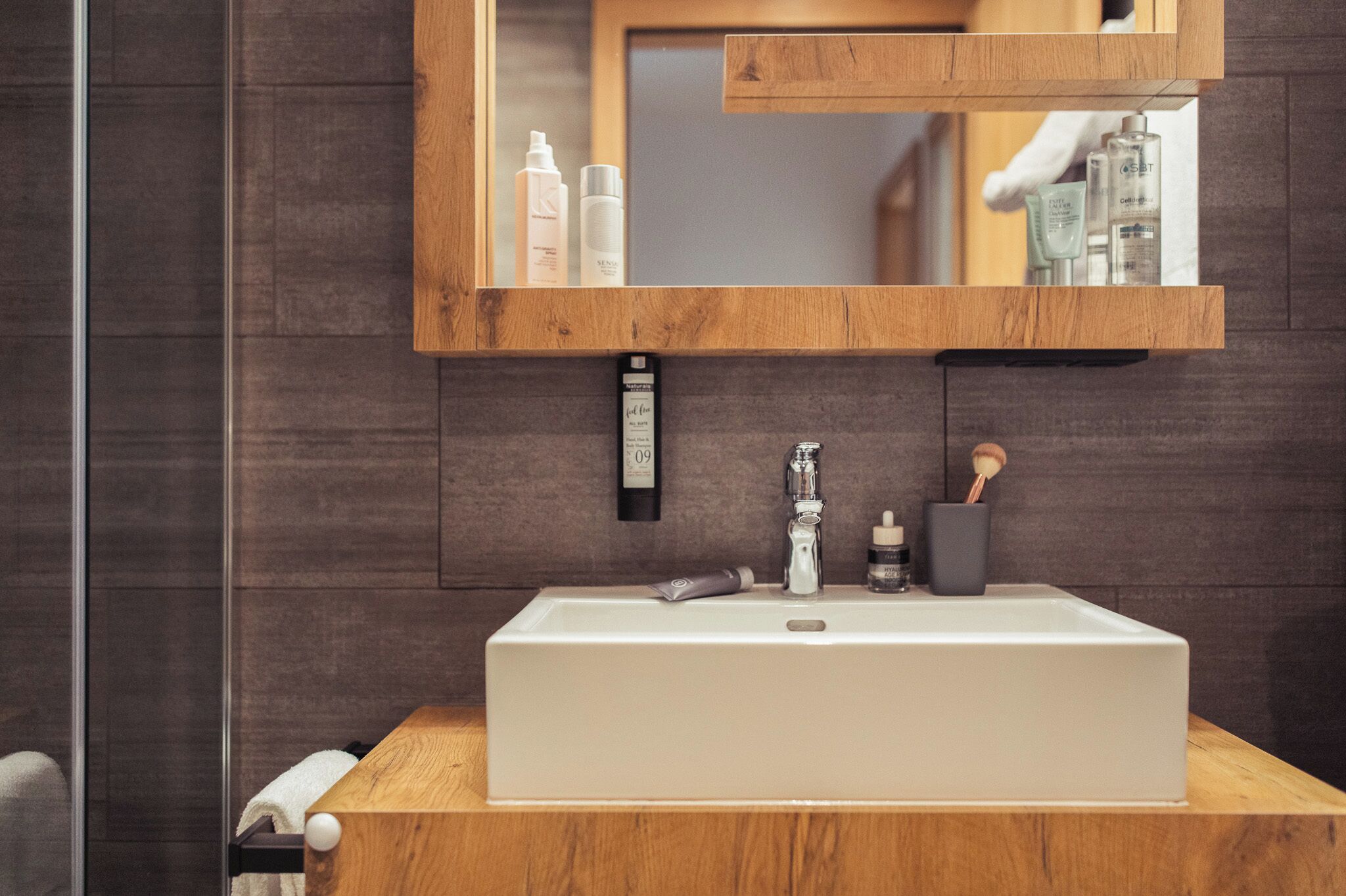 A bathroom with a wooden vanity, a white sink, and a mirror above it.