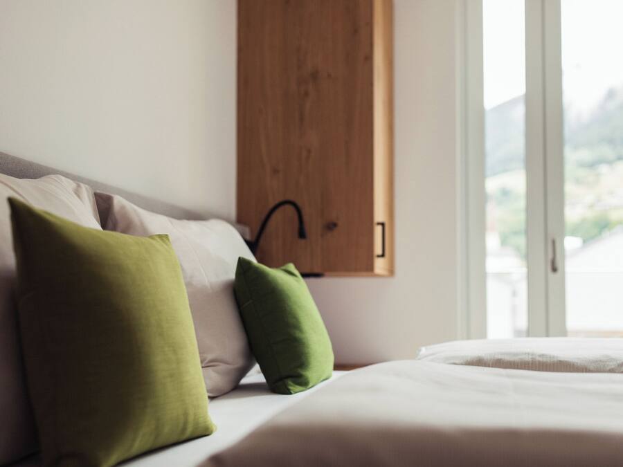 Uma cama com almofadas, um armário de madeira e uma janela com vista.