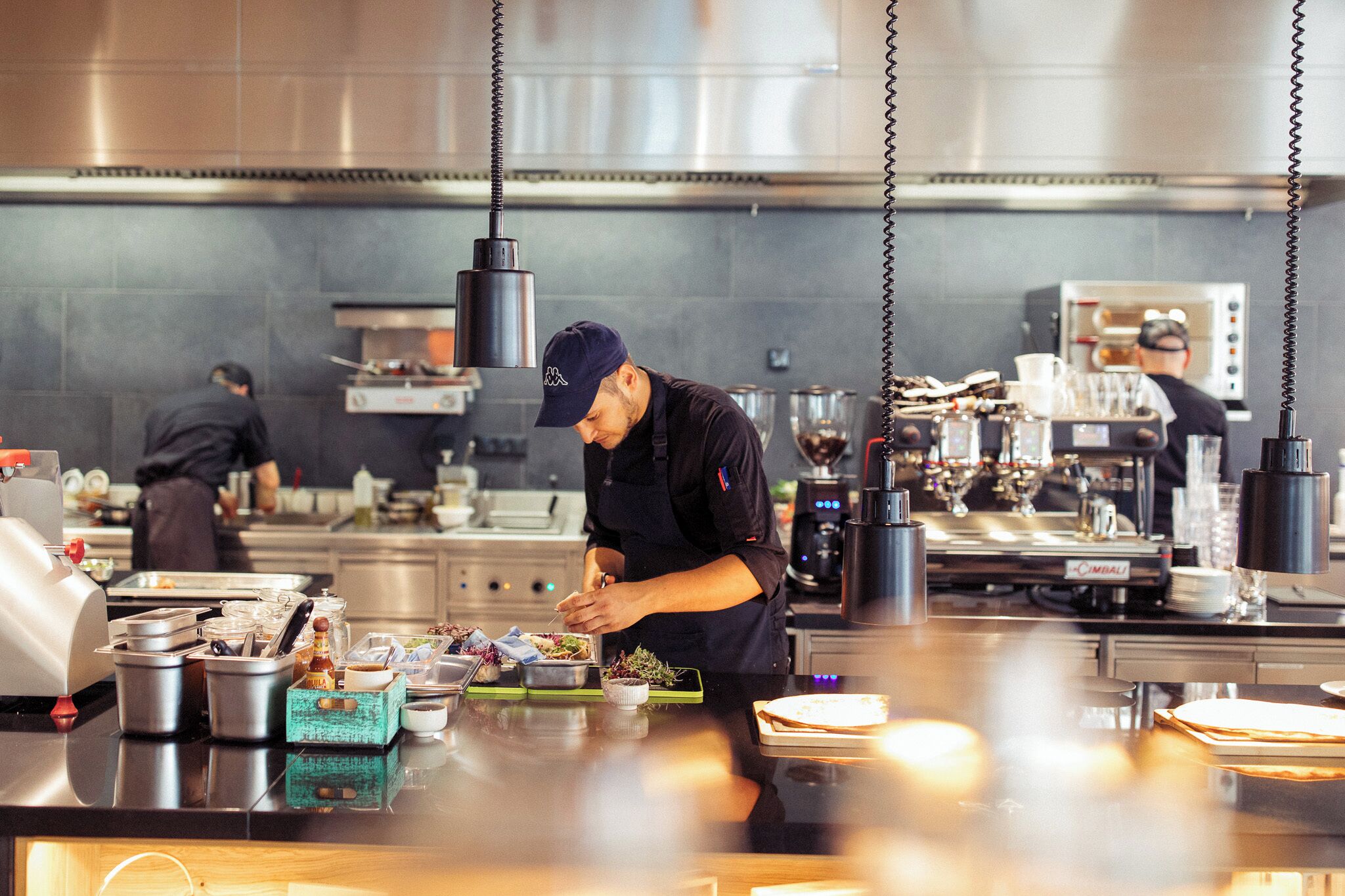 A commercial kitchen with stainless steel appliances, a chef preparing food, and various kitchen utensils and ingredients on the counter.