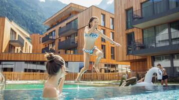 Una piscina con gente disfrutando del agua, rodeada de edificios modernos de madera con balcones.