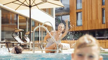 A swimming pool with a person jumping into the water, a lounge chair, and a modern building in the background.