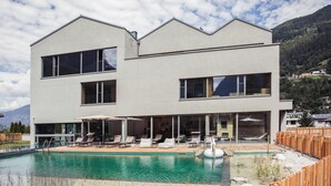 Un bâtiment moderne à deux étages doté d’une piscine, de chaises longues et d’une terrasse en bois.