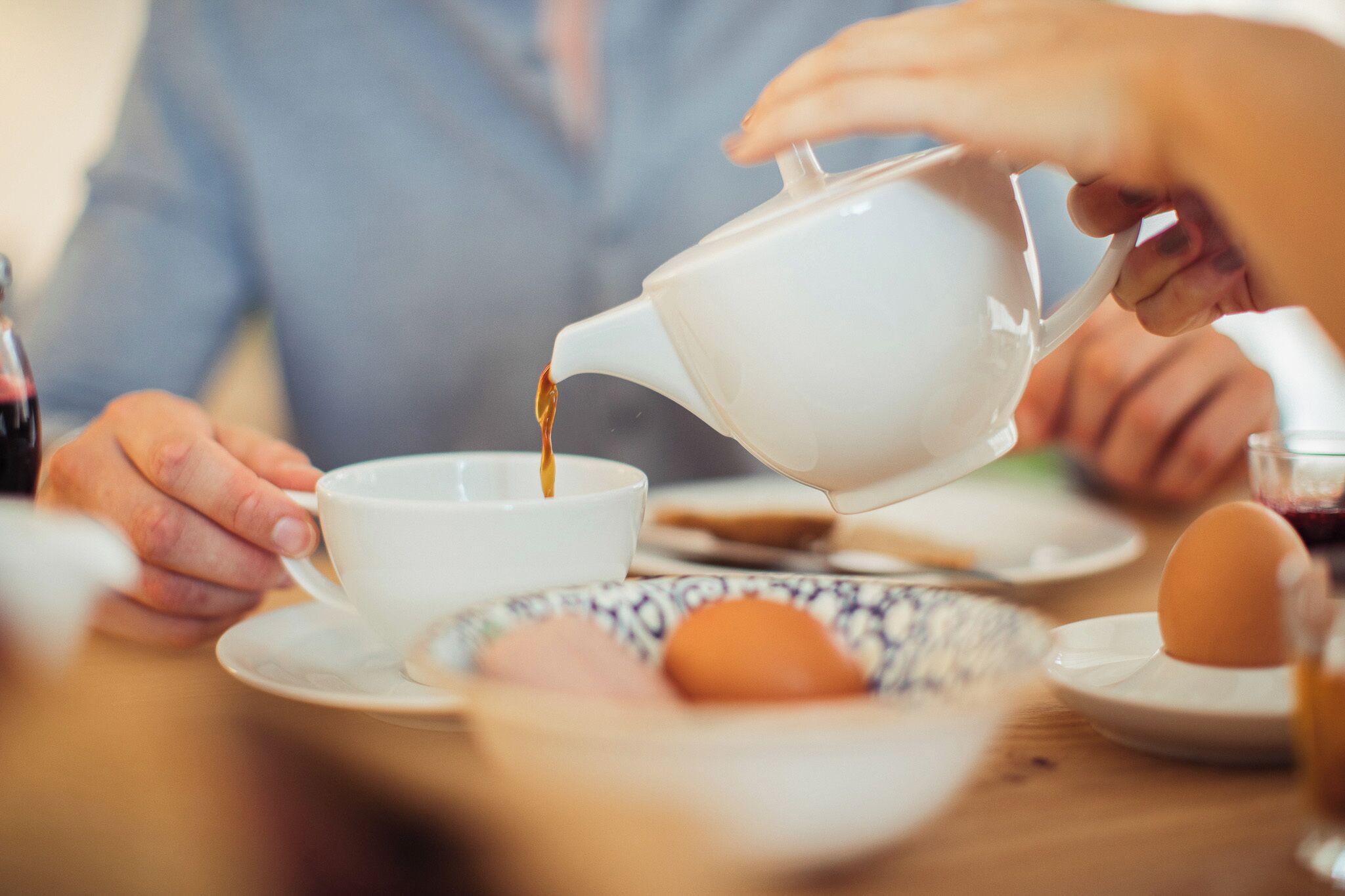 A person pouring a liquid from a teapot into a cup.
