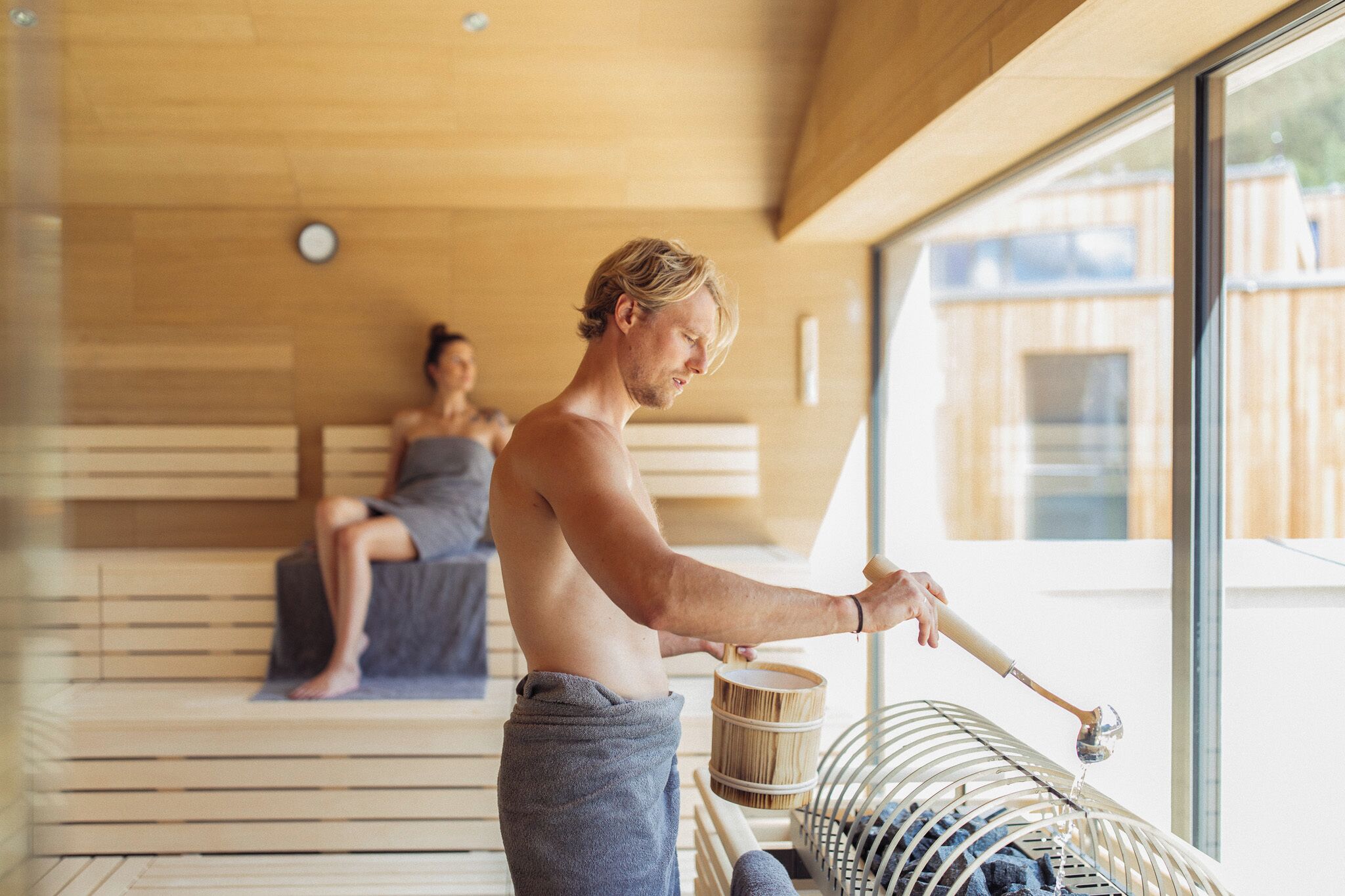 A sauna room with wooden benches and a person using a wooden mallet.