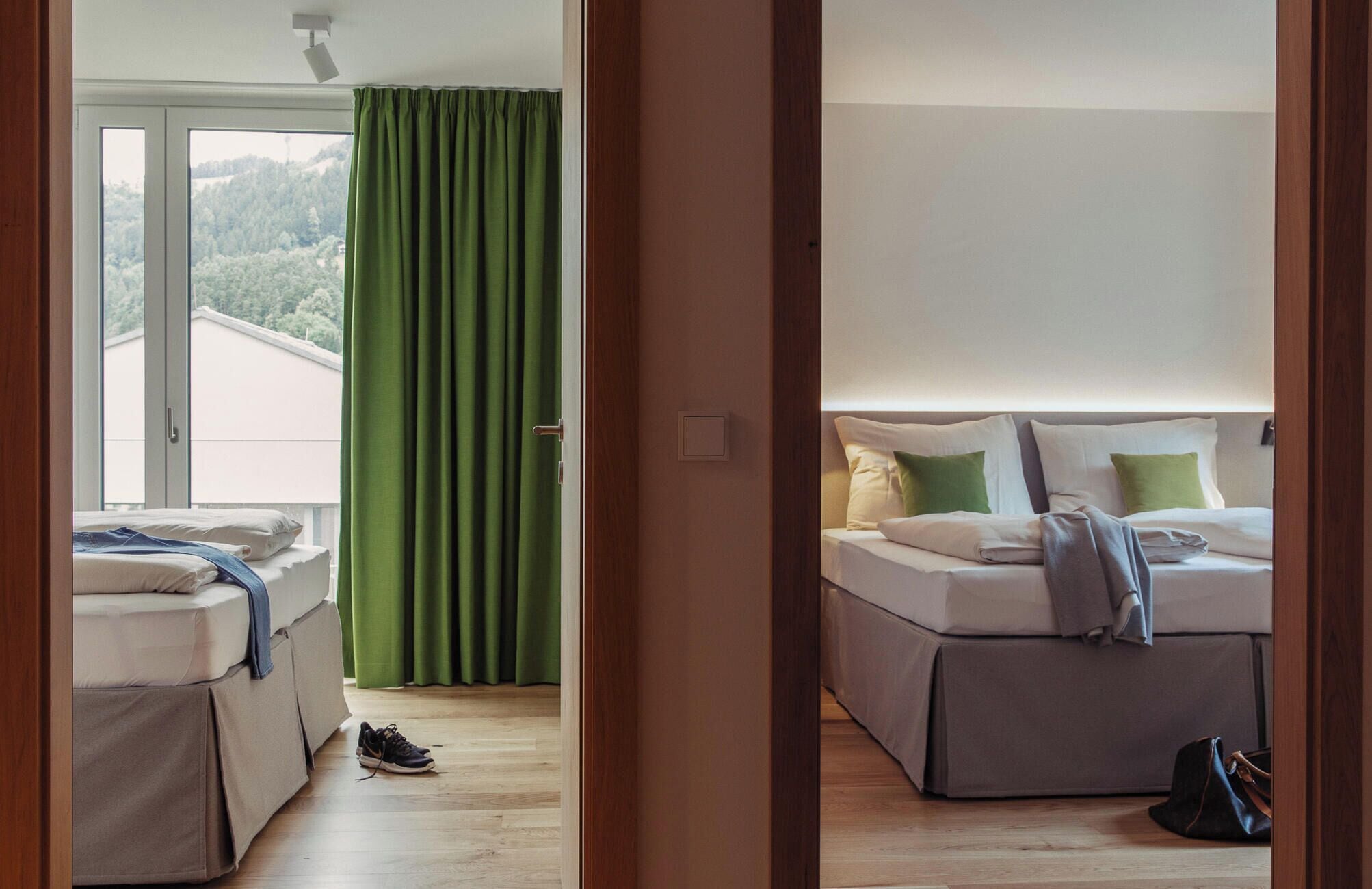 A hotel room with a bed, a window with curtains, a door, and a view of a forested area.